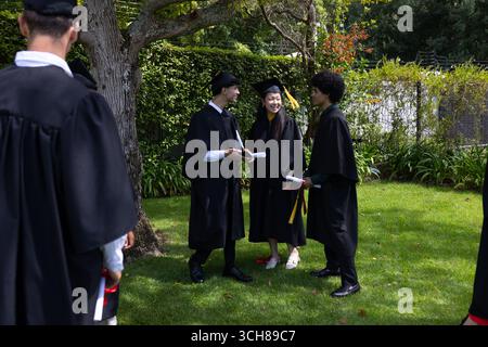 Celebrating graduation, diverse students in caps and gowns holding diplomas outdoors Stock Photo