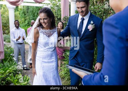 Bride and groom walking down aisle, smiling joyfully at outdoor wedding ceremony Stock Photo