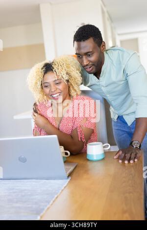 Couple enjoying video call on laptop at home, smiling and drinking coffee Stock Photo