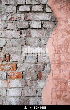Old, weathered brick wall with partially peeled pink stucco. Grunge vintage texture with damaged surface. Stock Photo
