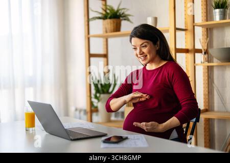 Young pregnant business woman, online teacher looking at laptop, online remote video call concept Stock Photo