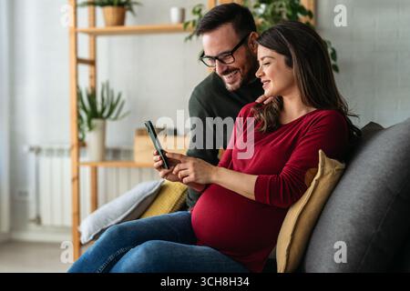 Happy young pregnant couple using virtual mobile service, online app on smart phone, Stock Photo