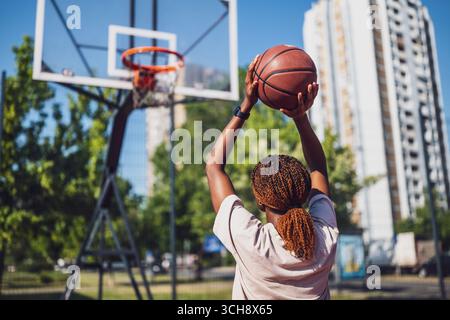 Young African American woman taking a basketball shot on an urban outdoor court during a sunny summer day. Stock Photo