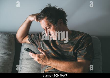 Middle-aged male using smartphone at home to explore social media content, low light, selective focus Stock Photo