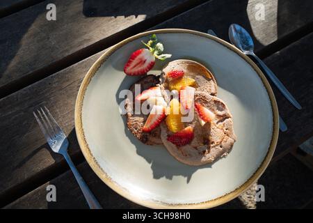 Buckwheat pancakes with fruit slices on a plate on a wooden table Stock Photo