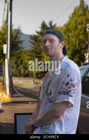 Young man in a floral shirt stands on a street corner Stock Photo