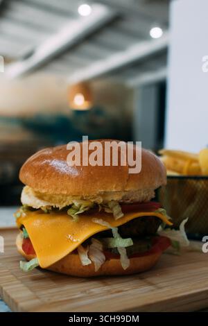 burger with melted cheddar cheese, vegetables and fried potatoes Stock Photo