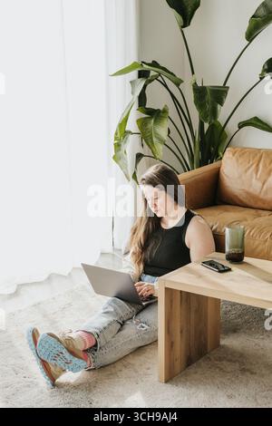 Middle aged woman sits on floor while working on laptop computer Stock Photo
