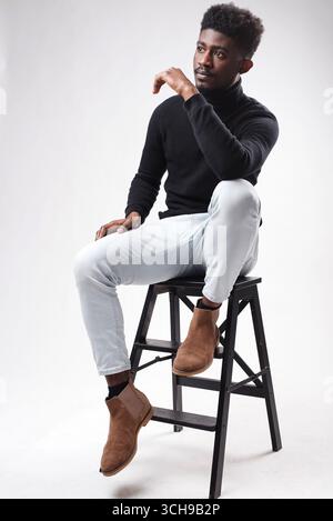 Relaxed curly bearded dark guy in casual outfit sitting at armchair Stock Photo