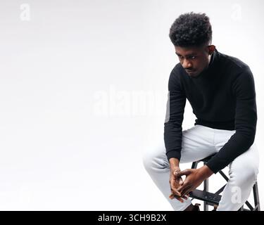 Relaxed curly bearded dark guy in casual outfit sitting at armchair Stock Photo