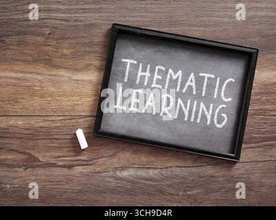 Thematic learning message handwritten with white chalk on a small blackboard laying on a wooden desk Stock Photo