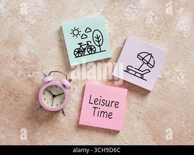 Pink alarm clock alongside colorful sticky notes featuring drawings of cycling and beach relaxation, highlighting leisure and work-life balance Stock Photo