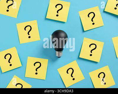 Black light bulb surrounded by many question marks on sticky notes. Surrounded by problems. Failure to solve problems concept. Stock Photo