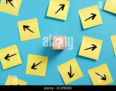 Wooden cube with question mark and arrows drawn on sticky notes pointing in different directions, representing possible choices and decision making Stock Photo