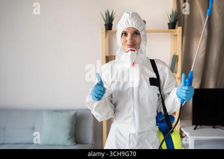 Female exterminator from pest control service working inside house with sprayer bottle showing like thumbs-up gesture at home. copy space Stock Photo