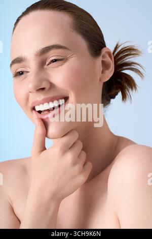 A young, stylish woman beams while playfully resting her chin on her hand. Stock Photo