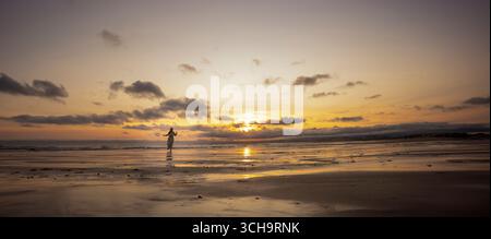 Woman walking on the beach at sunset with cloudy sky Stock Photo