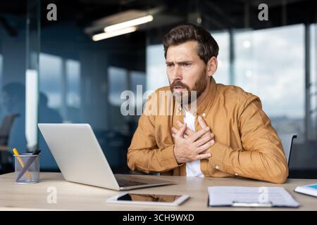 Stressed office worker experiencing chest pain and breathing problems, suffering from heart attack or panic attack after reading bad news on computer Stock Photo
