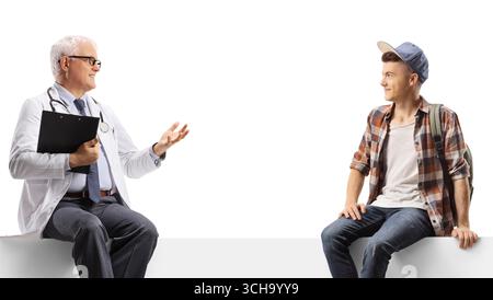 Mature male doctor talking to a teenage male student seated on a blank panel isolated on white background Stock Photo