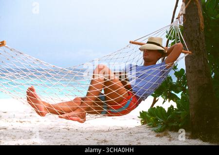 Maldives. Young man relaxing in hammock on tropical beach. Stock Photo