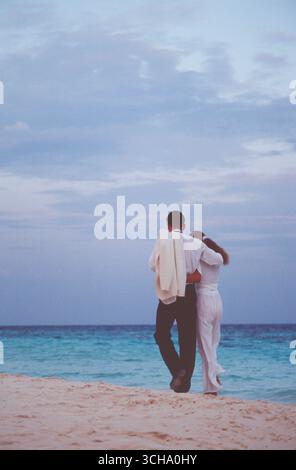Maldives. Young couple in evening clothes, back view, walking on tropical beach. Stock Photo