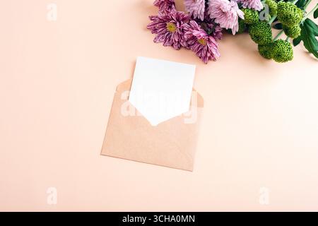 Brown envelope with blank card and pink chrysanthemums on pastel background, floral mockup for message or invitation. Top view, flat lay. Stock Photo