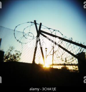 Setting sun behind a fence of barbed wire Stock Photo - Alamy