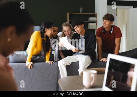 Diverse teens gathered on couch, reading college acceptance letter, celebrating success, at home. diverse teenagers, celebration, happiness, achieveme Stock Photo