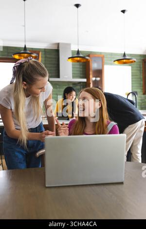 Collaborating in kitchen, teen diverse friends sharing ideas enthusiastically on laptop, at home. Teamwork, brainstorming, friendship, diverse teenage Stock Photo