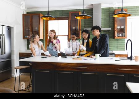 Collaborating on school project, teen diverse friends sharing ideas in modern kitchen, at home. Friendship, teamwork, brainstorming, creativity, colla Stock Photo