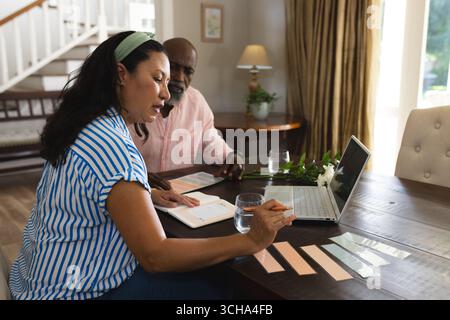 Planning celebration, senior diverse couple using laptop and notes at home, discussing details. computer, discussion, relationships Stock Photo
