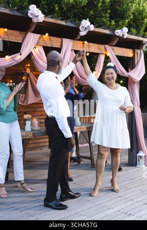 At wedding, Senior couple dancing joyfully at outdoor celebration with friends clapping. happiness, party, elderly, outdoors Stock Photo