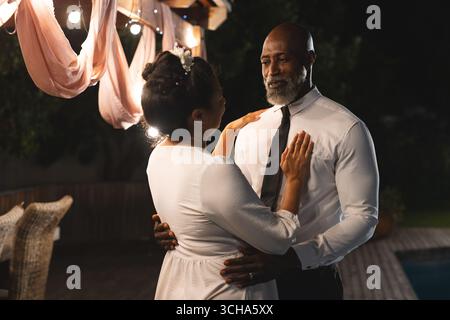 At wedding, Dancing under string lights, senior couple sharing joyful moment at outdoor celebration. happiness, elderly, romance, party Stock Photo