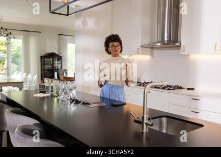 In modern kitchen, woman drying glassware while preparing for event, at home. chores, preparation, domestic, household, organization, homemaking Stock Photo