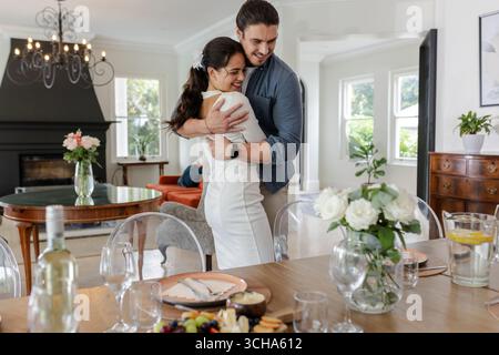 Couple embracing happily in elegant dining room with table set for celebration, at home. romance, party, elegance, love, happiness, togetherness Stock Photo