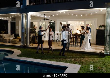 Celebrating joyfully, guests at outdoor wedding reception near pool with string lights. celebration, festive, poolside Stock Photo