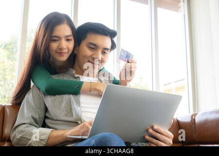 A young couple shopping online at home together, using a credit card for purchases, illustrating modern e-commerce, convenience, and lifestyle Stock Photo