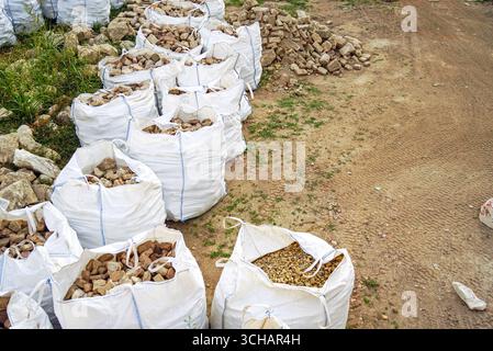 Natural stones, pebbles and old bricks in white bulk bags for landscape design projects. Garden construction materials and rockery building supplies Stock Photo