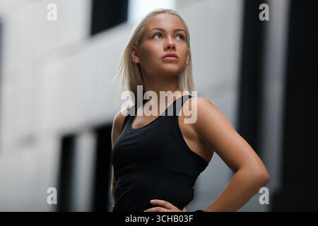 Confident athletic woman posing outdoors in black top, modern city setting Stock Photo