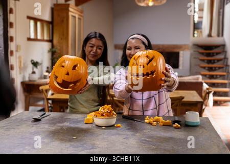 Halloween time, carving pumpkins together, grandmother and asian female teenager having fun, at home. halloween, celebration, family, tradition, autum Stock Photo