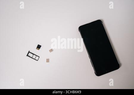 Sim cards and memory card positioned near sleek smartphone on white surface, representing mobile technology connectivity and potential device Stock Photo