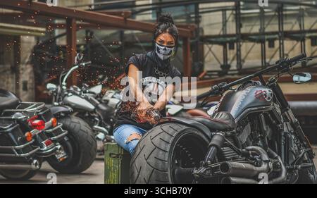 Woman with face scarf using an angle grinder on a custom Harley motorcycle Stock Photo