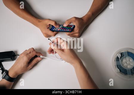 Top view of two technicians connecting RGB led strip lights using remote control and controller, adjusting backlight settings for customized Stock Photo