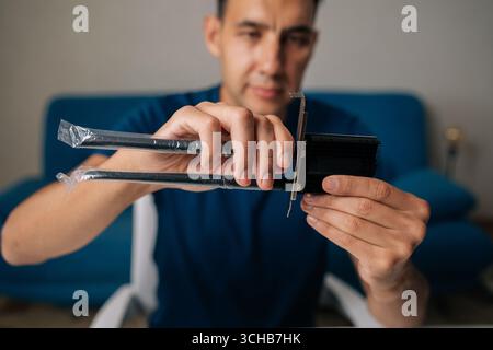 Selective focus portrait of technician male assembling wi-fi module by connecting antennas sitting at white table in home office, focused on ensuring Stock Photo