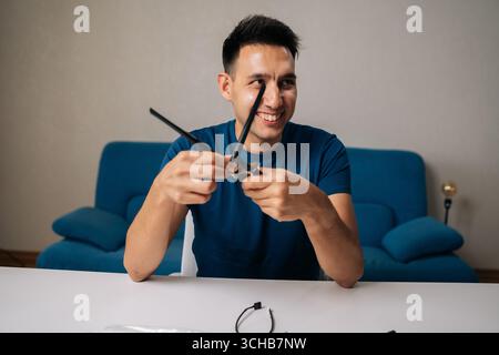Portrait of smiling technician male assembling wi-fi module by connecting antennas sitting at white table in home office, focused on ensuring optimal Stock Photo