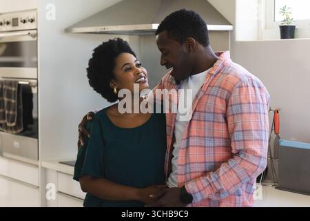 Smiling African American couple standing in modern kitchen, with stainless steel oven. Romance, intimacy, harmony, contemporary, warmth, domestic, aff Stock Photo