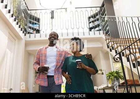 Smiling African American couple leaning toward each other in bright home foyer, holding coffee cups. Romance, intimacy, cozy, domestic, lifestyle, arc Stock Photo