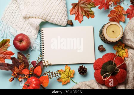 Autumn flat lay background. Falling leaves, notenad, knitted scarf and wooden candle on blue background. Stock Photo