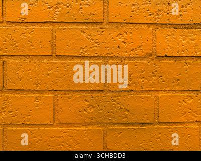 Close-up of an orange-painted brick wall with visible texture and rough surface, ideal for use as a background or urban design element. Stock Photo
