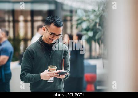 Smiling businessman professional surfing through smart phone while standing in convention center Stock Photo